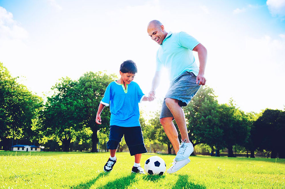 SIS father son playing soccer park summer concept PNQ6YYW